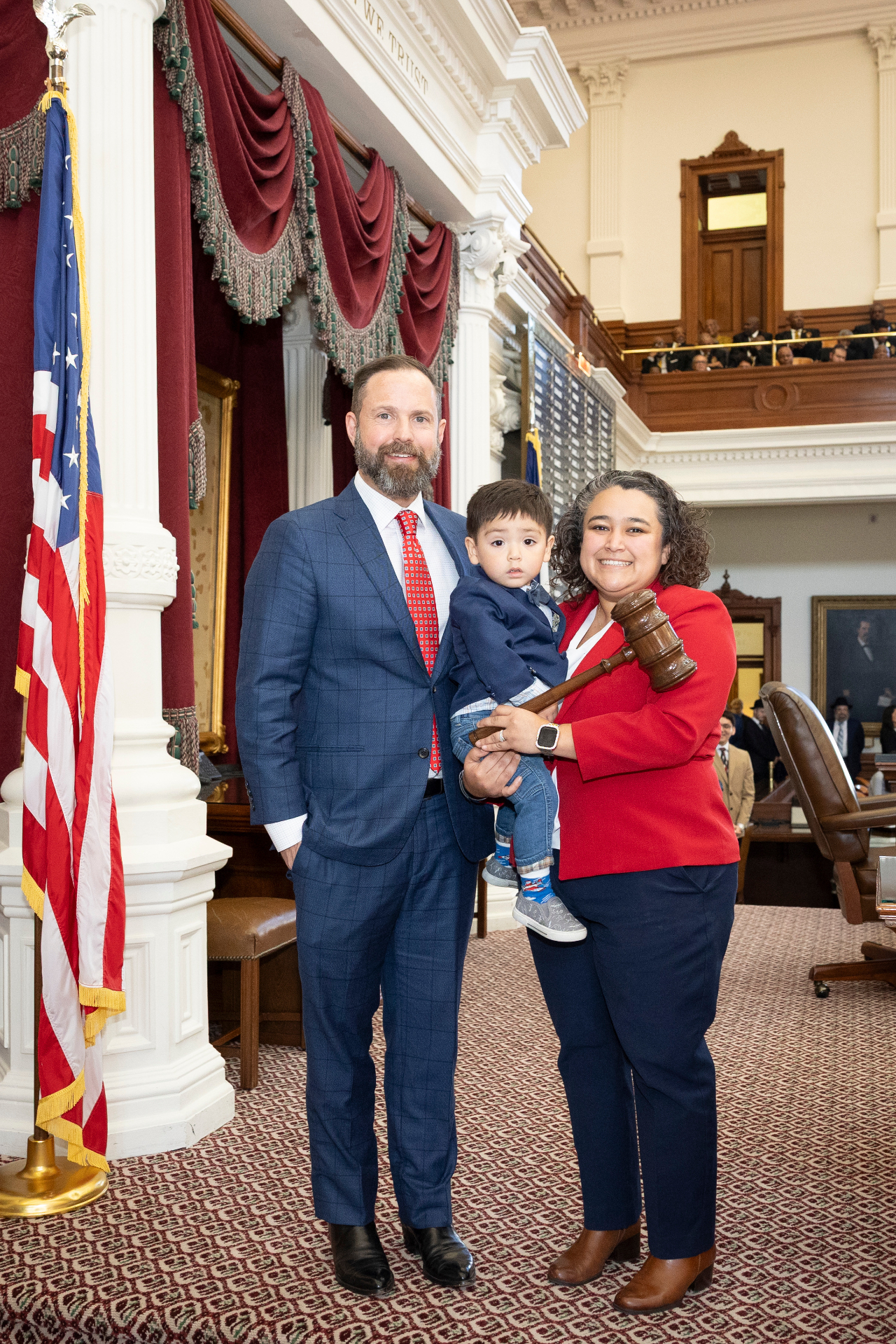 Denise with her husband Ruben and son Zeke in front of the American flag on the Texas House floor.